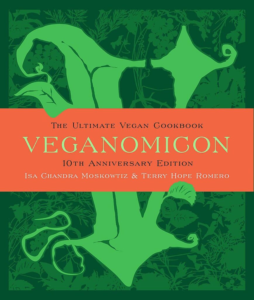  Veganomicon cookbook next to a variety of prepared vegan dishes